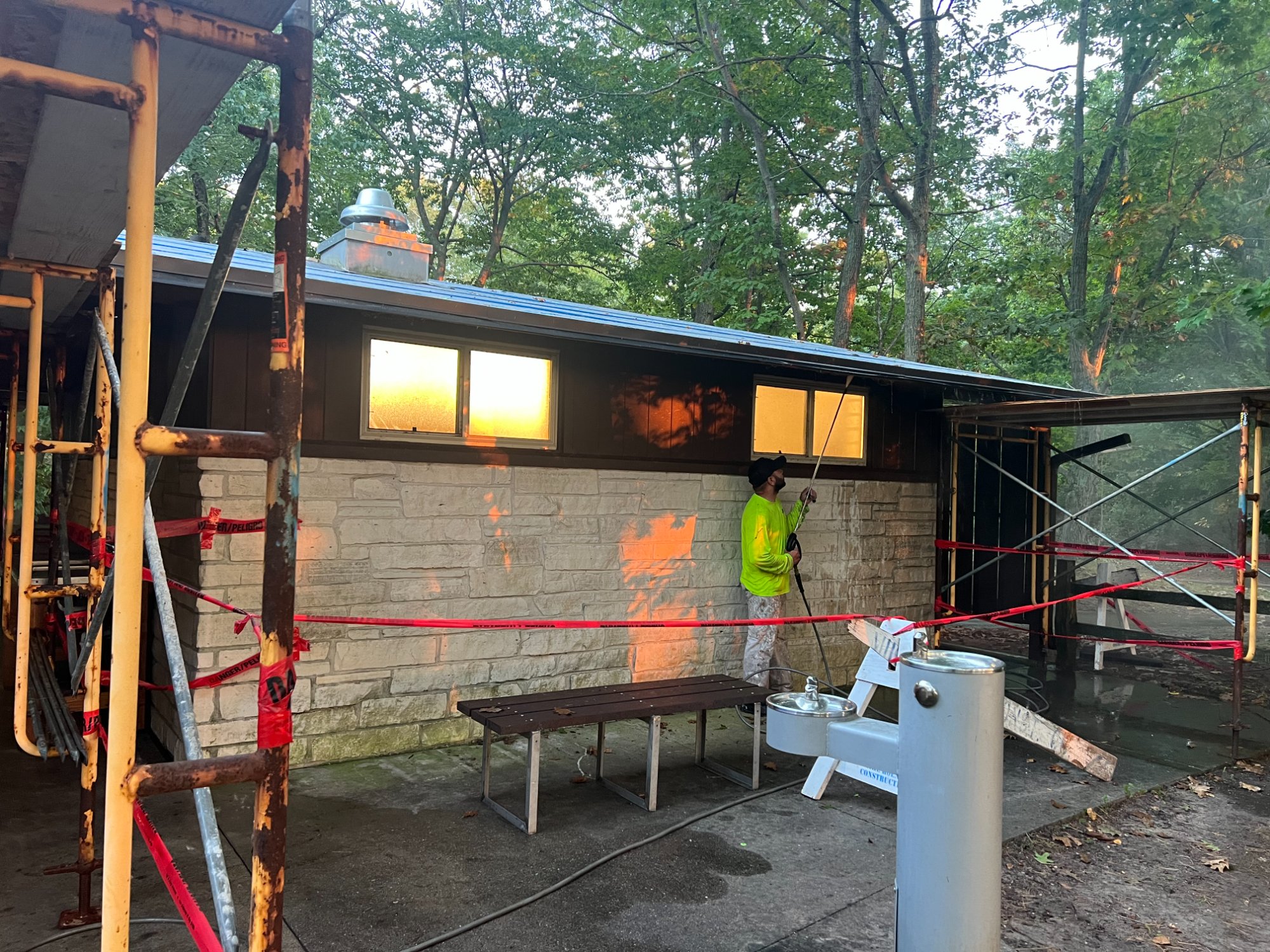 Worker in safety vest power washing stone and wood exterior of municipal park building