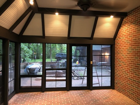 Screened porch with dark painted beams, glass panels, brick floor, and ceiling fan