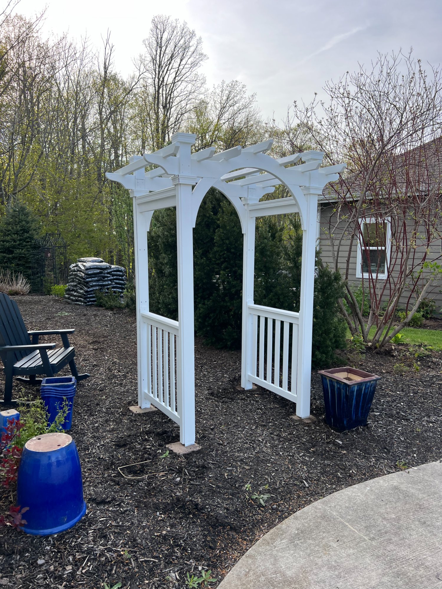 Freshly painted white garden arbor with decorative brackets in backyard landscape