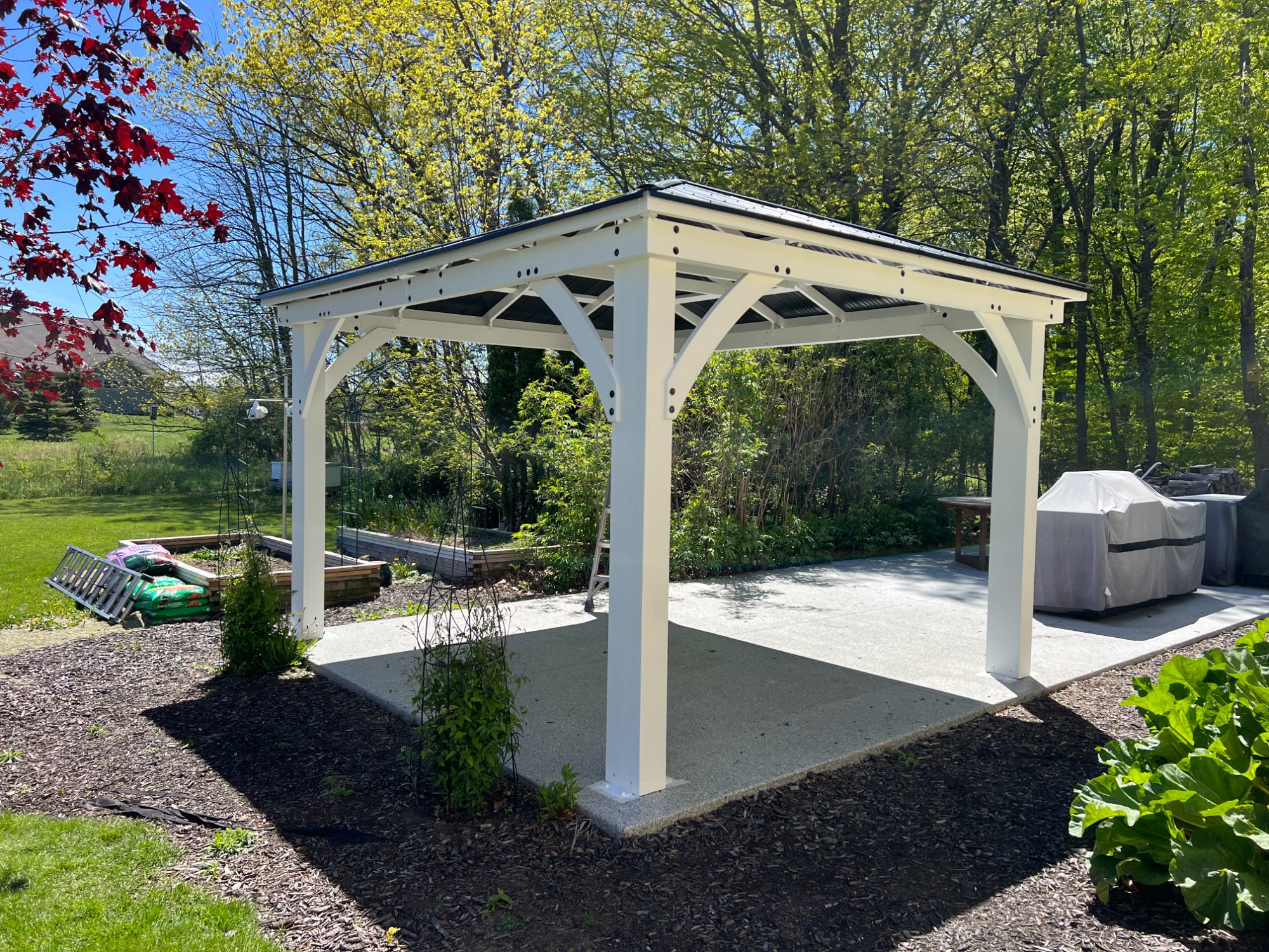 White painted outdoor pavilion with dark metal roof and decorative bracket work in backyard