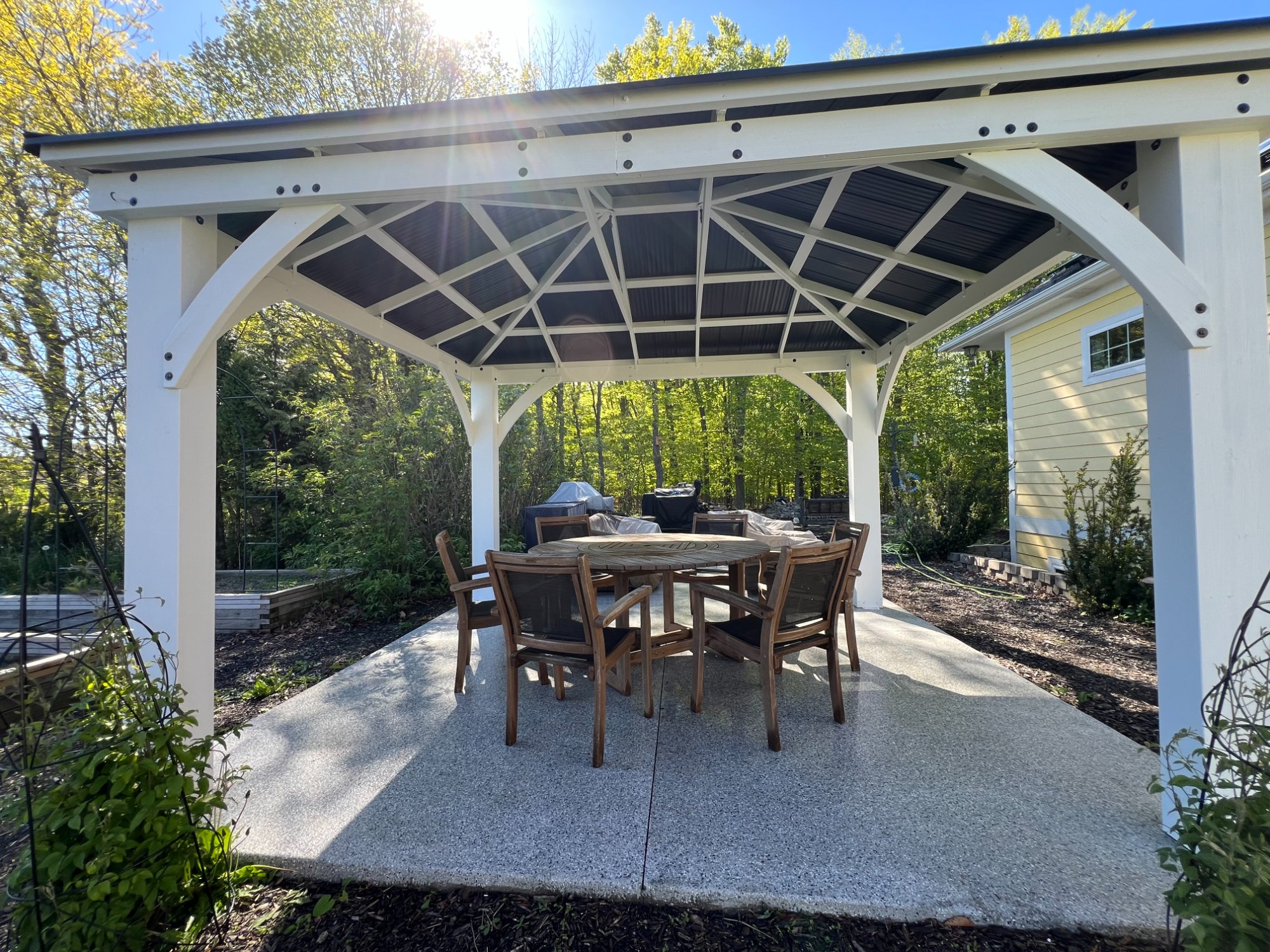 View from under white painted outdoor pavilion showing decorative roof framing and dining area