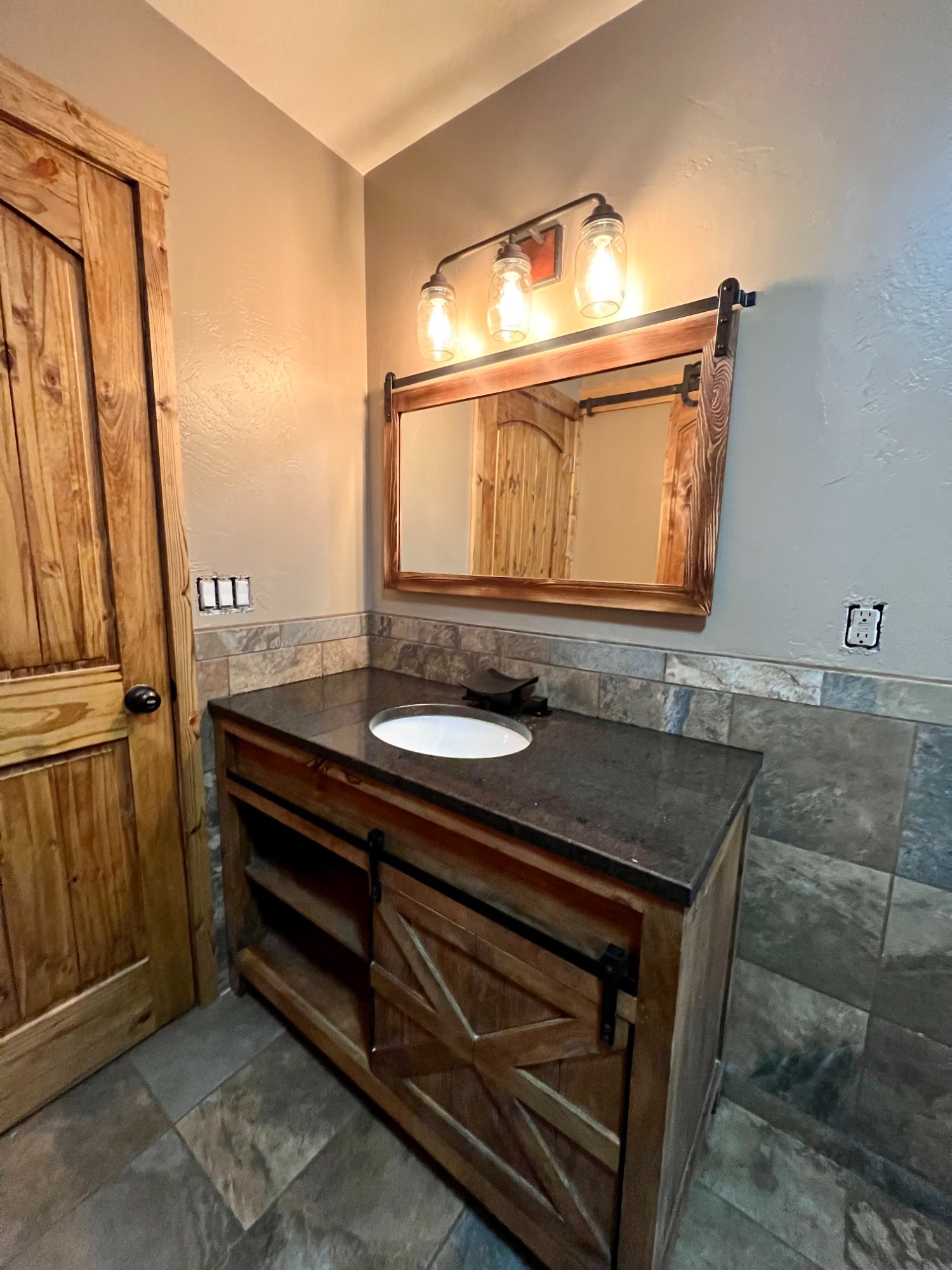 Rustic bathroom with stained wood barn door vanity, wood-framed mirror, and mason jar light fixtures