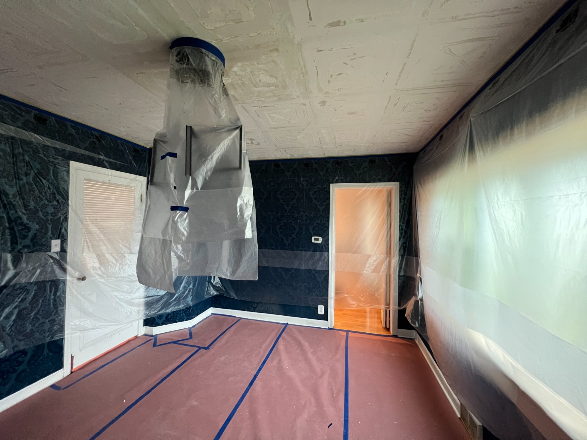Room with plastic sheeting protecting dark wallpaper and floors during ceiling drywall repair and painting