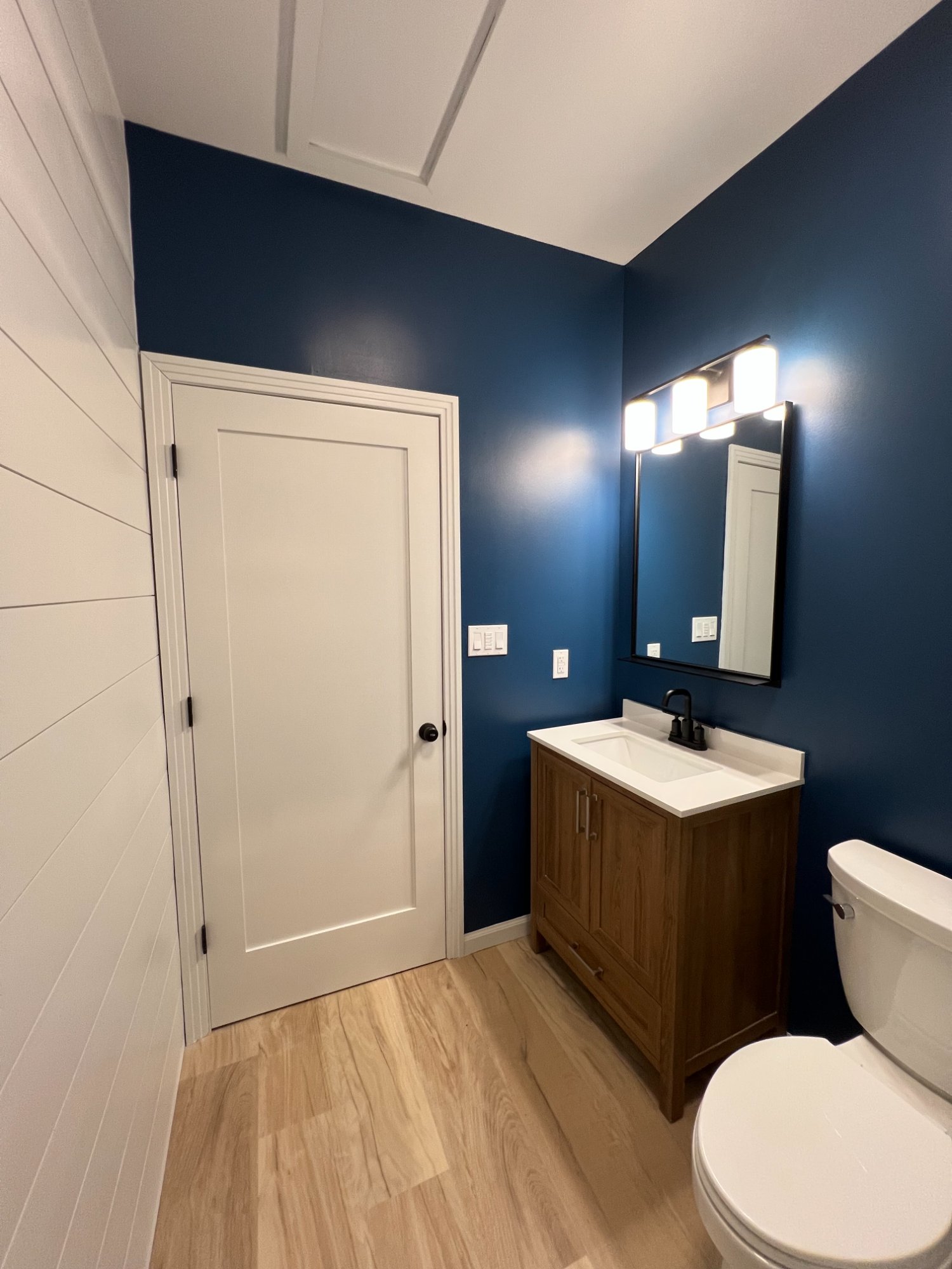 Modern powder room with deep navy blue walls, white shiplap accent wall, and white door