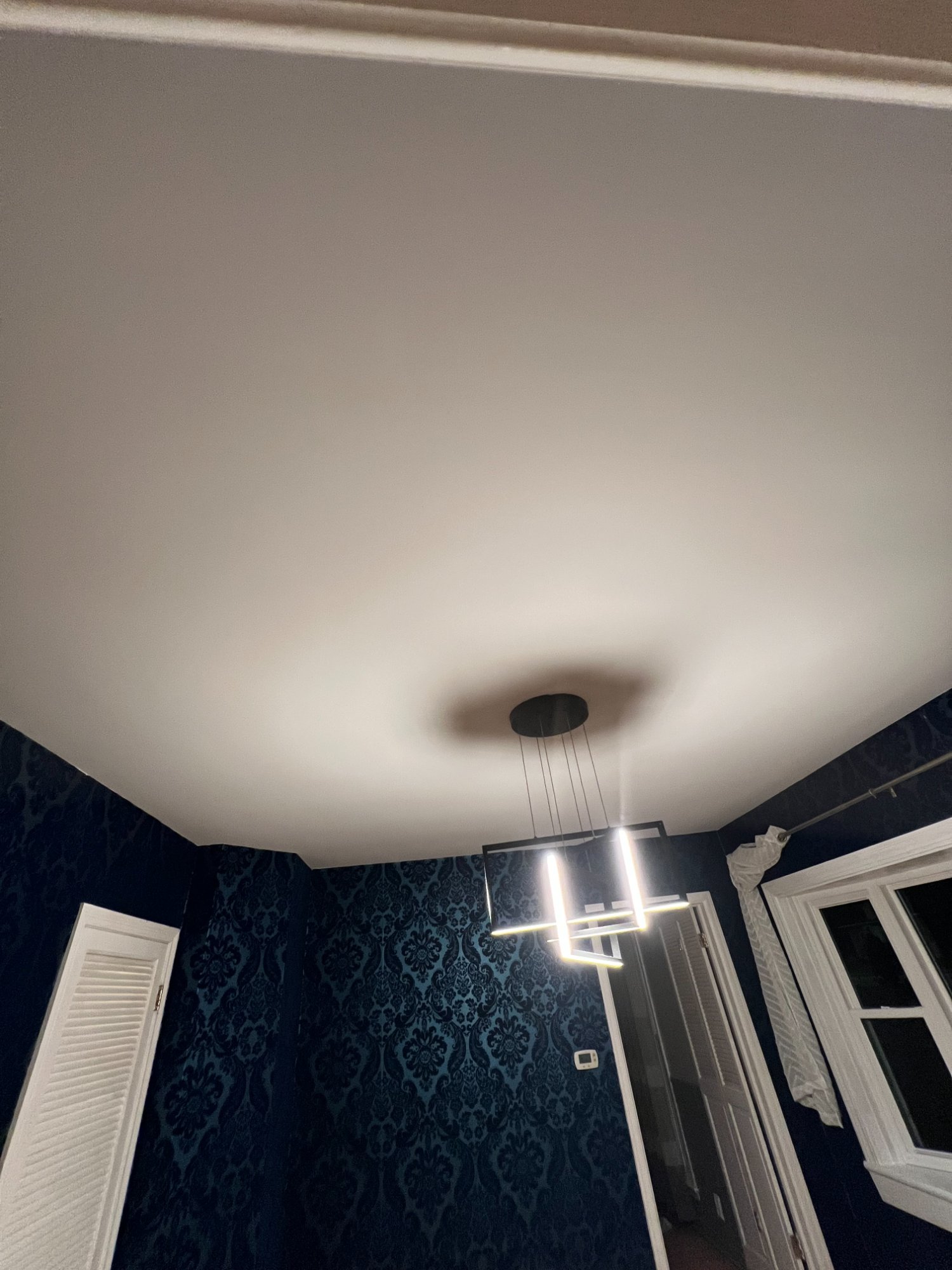 Freshly repainted smooth white ceiling in room with dark blue damask wallpaper and modern pendant light
