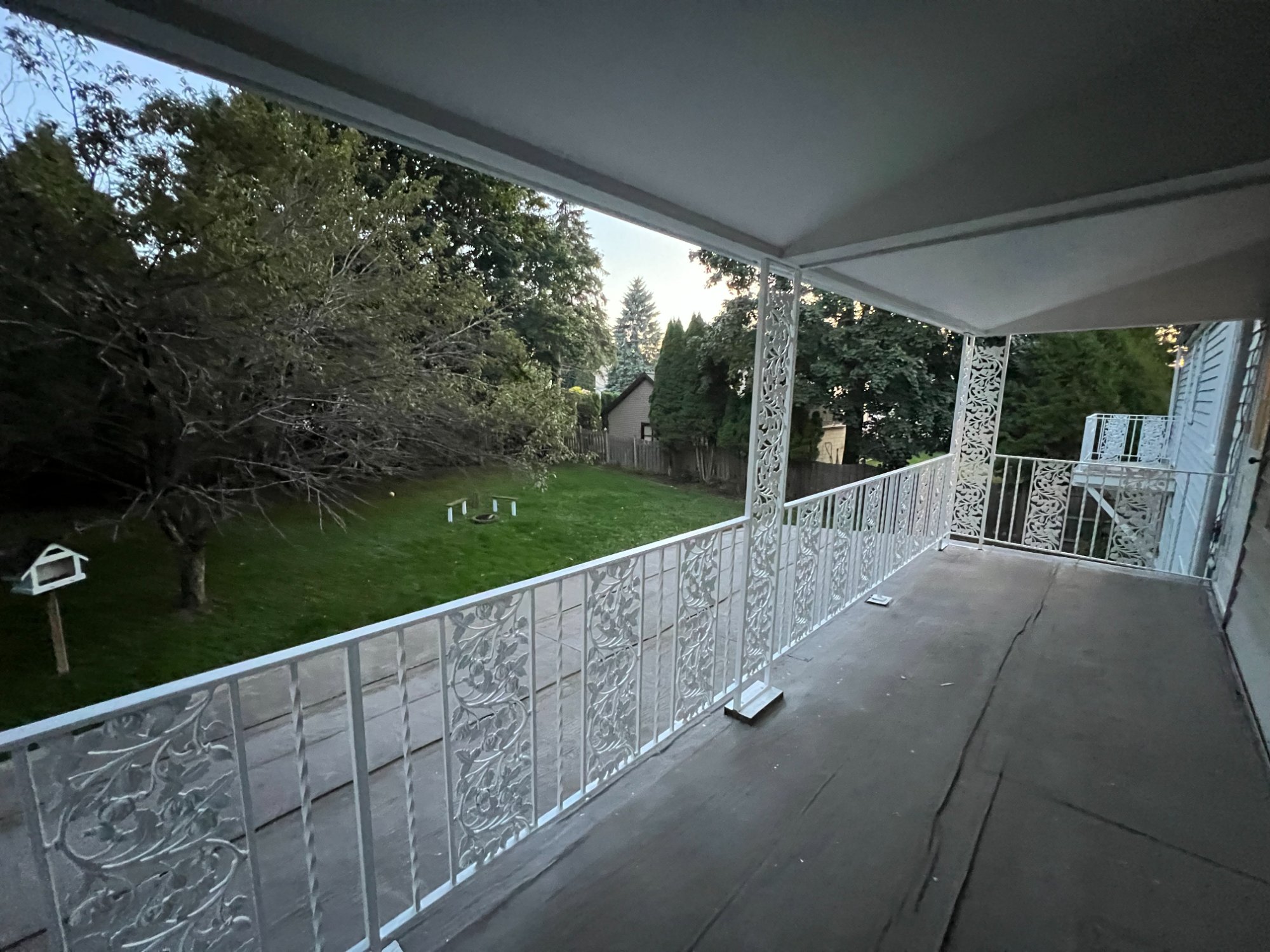 Freshly painted white ornamental iron balcony railing with scroll work overlooking backyard