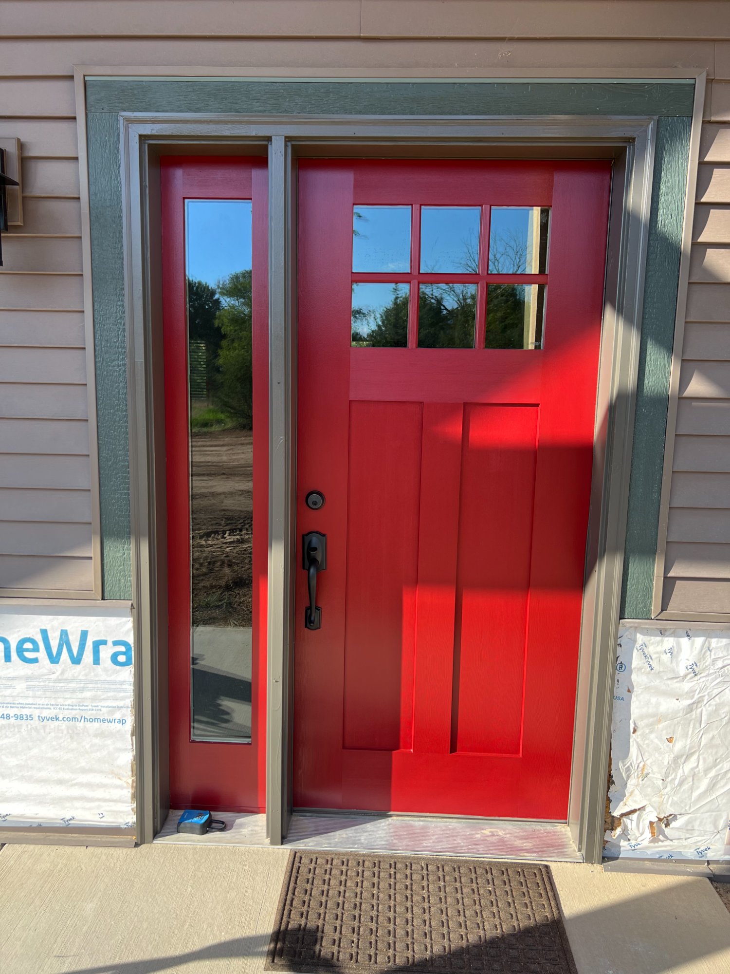 Freshly painted bold red craftsman-style front door with sidelite panel on new construction
