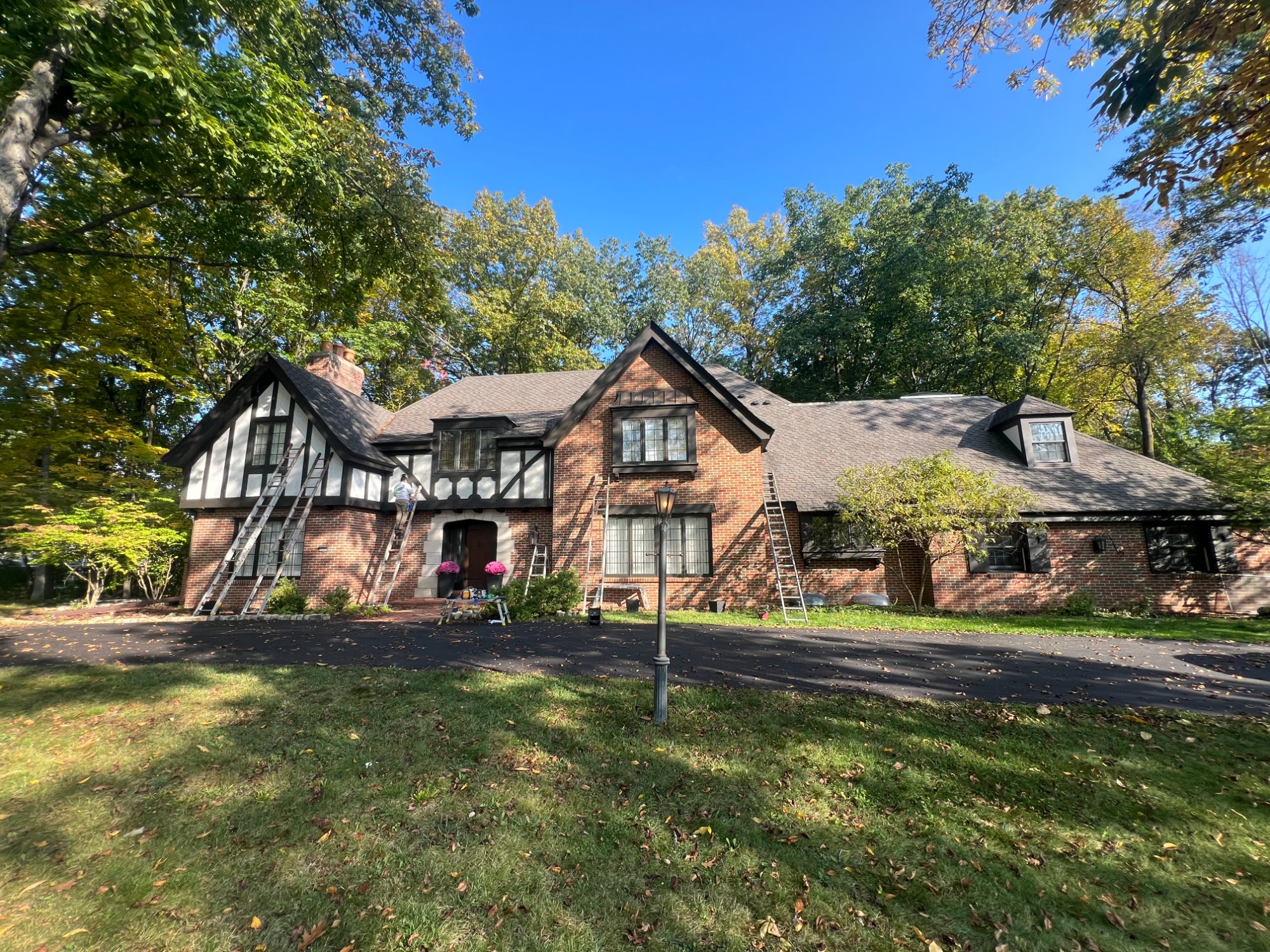 Large Tudor-style brick estate with ladders set up during exterior timber framing painting