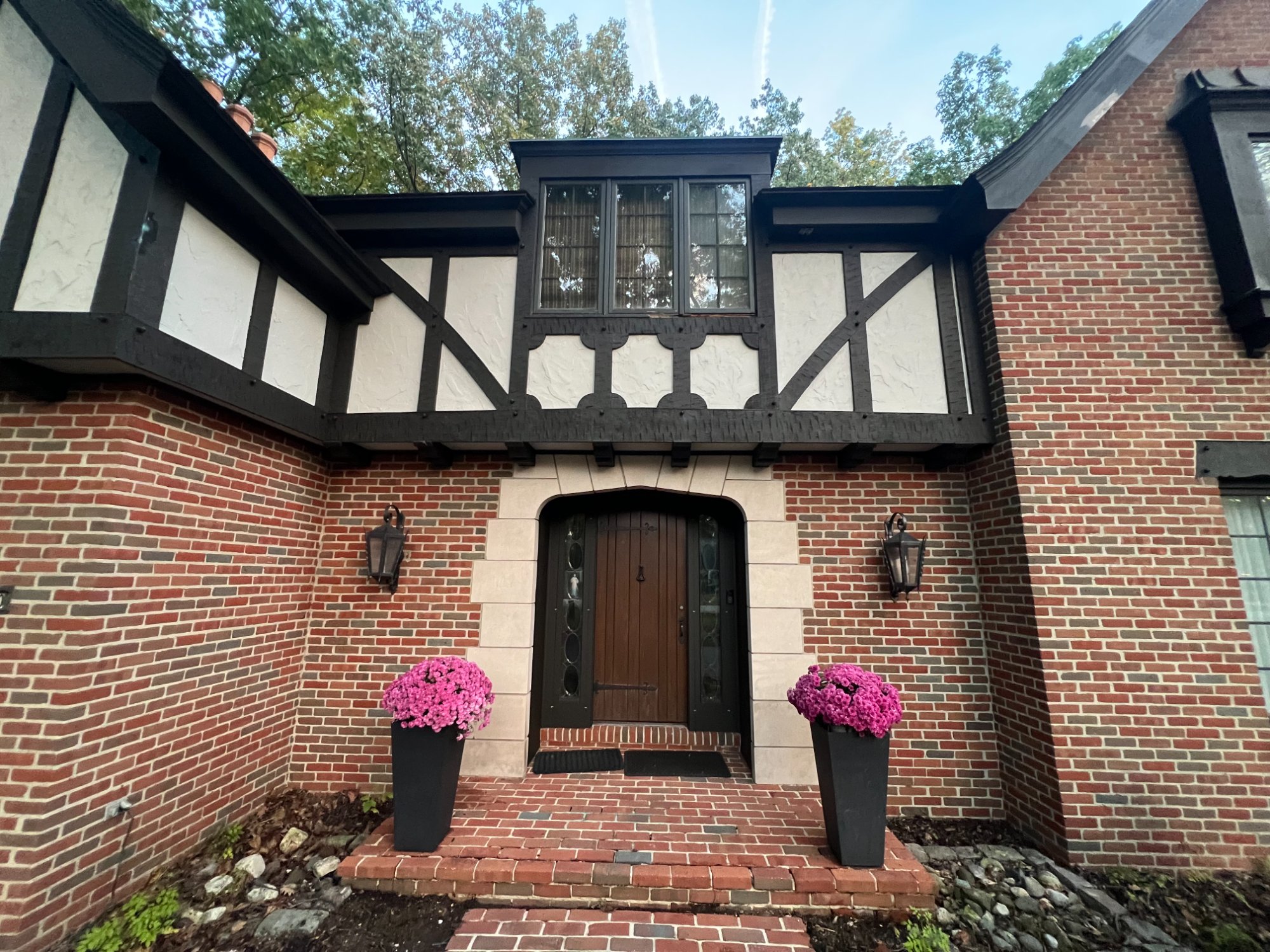 Close-up of Tudor entryway with freshly painted dark timber framing, cream stucco, and arched wood door