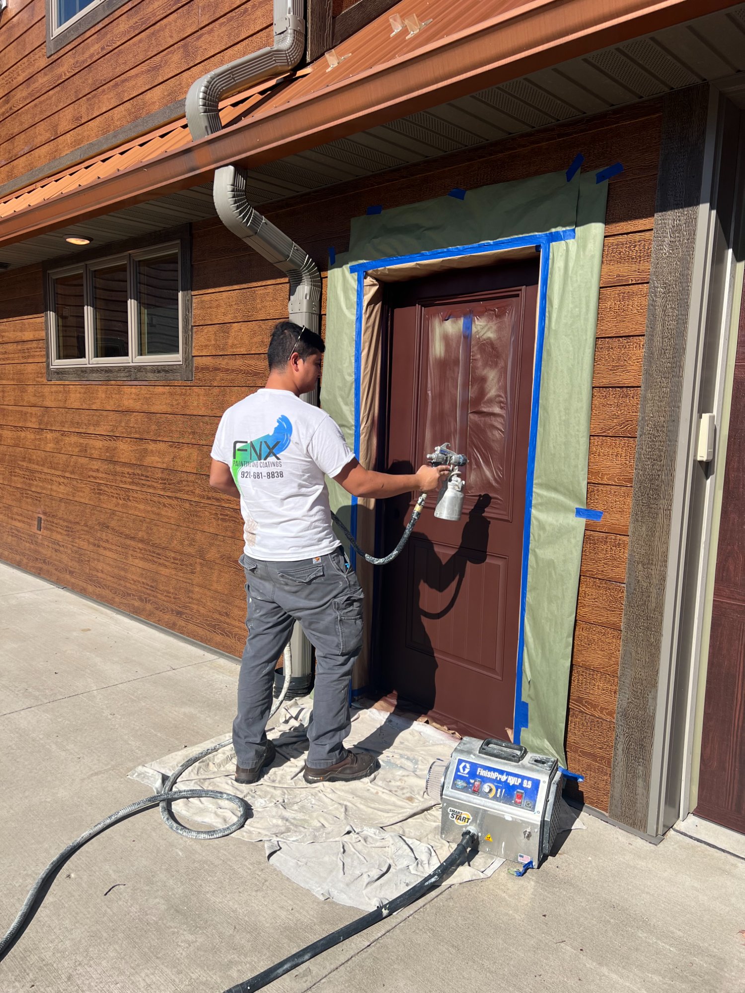 Painter using HVLP spray gun to paint front door with precision masking and drop cloths