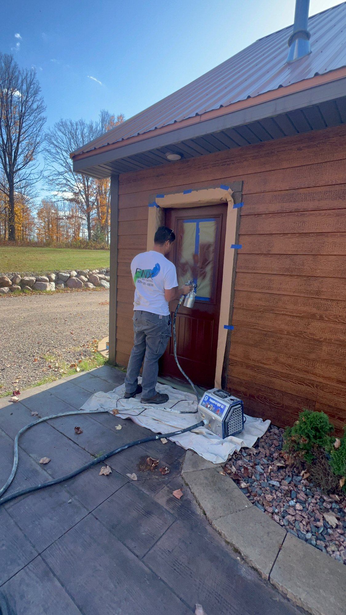 Painter spray painting side entry door with professional equipment, masking tape, and drop cloth protection