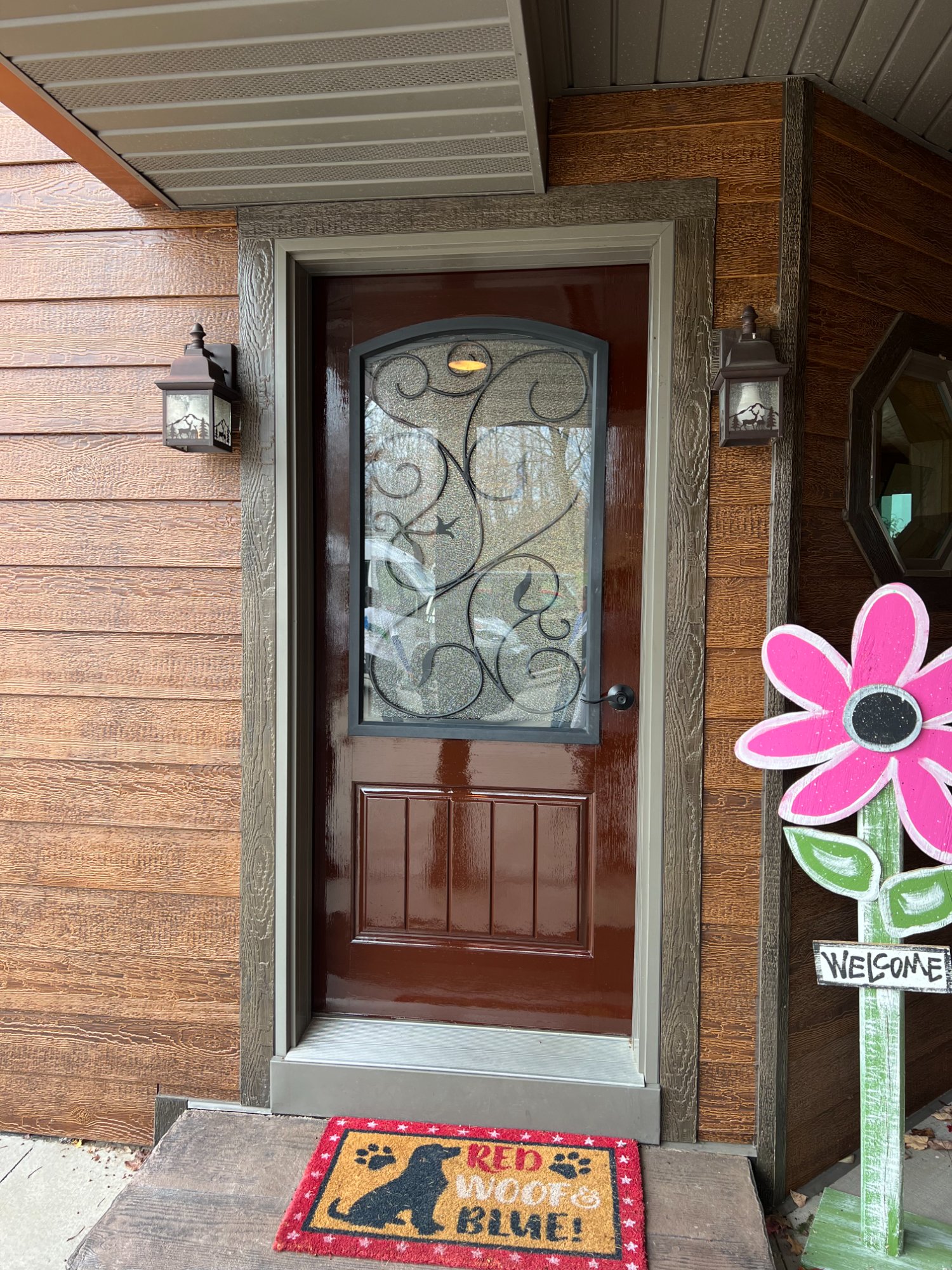 Beautifully refinished front door with decorative ironwork glass on wood-sided home, close-up view