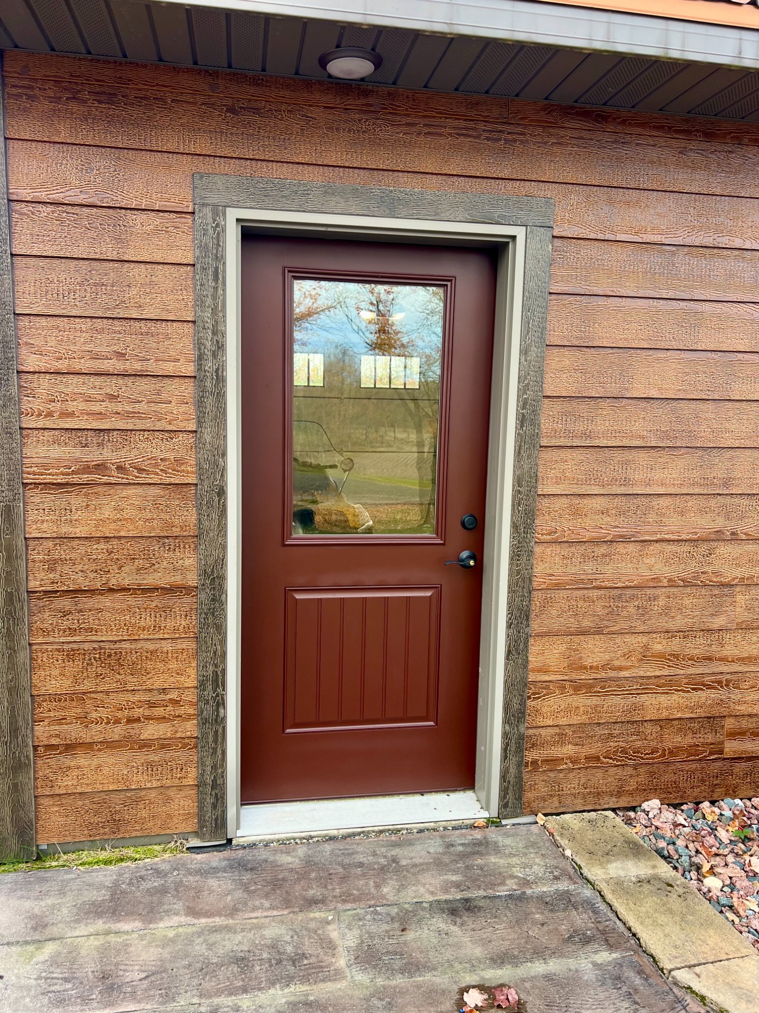 Freshly painted garage entry door in matching brown with half-glass panel on wood-sided building
