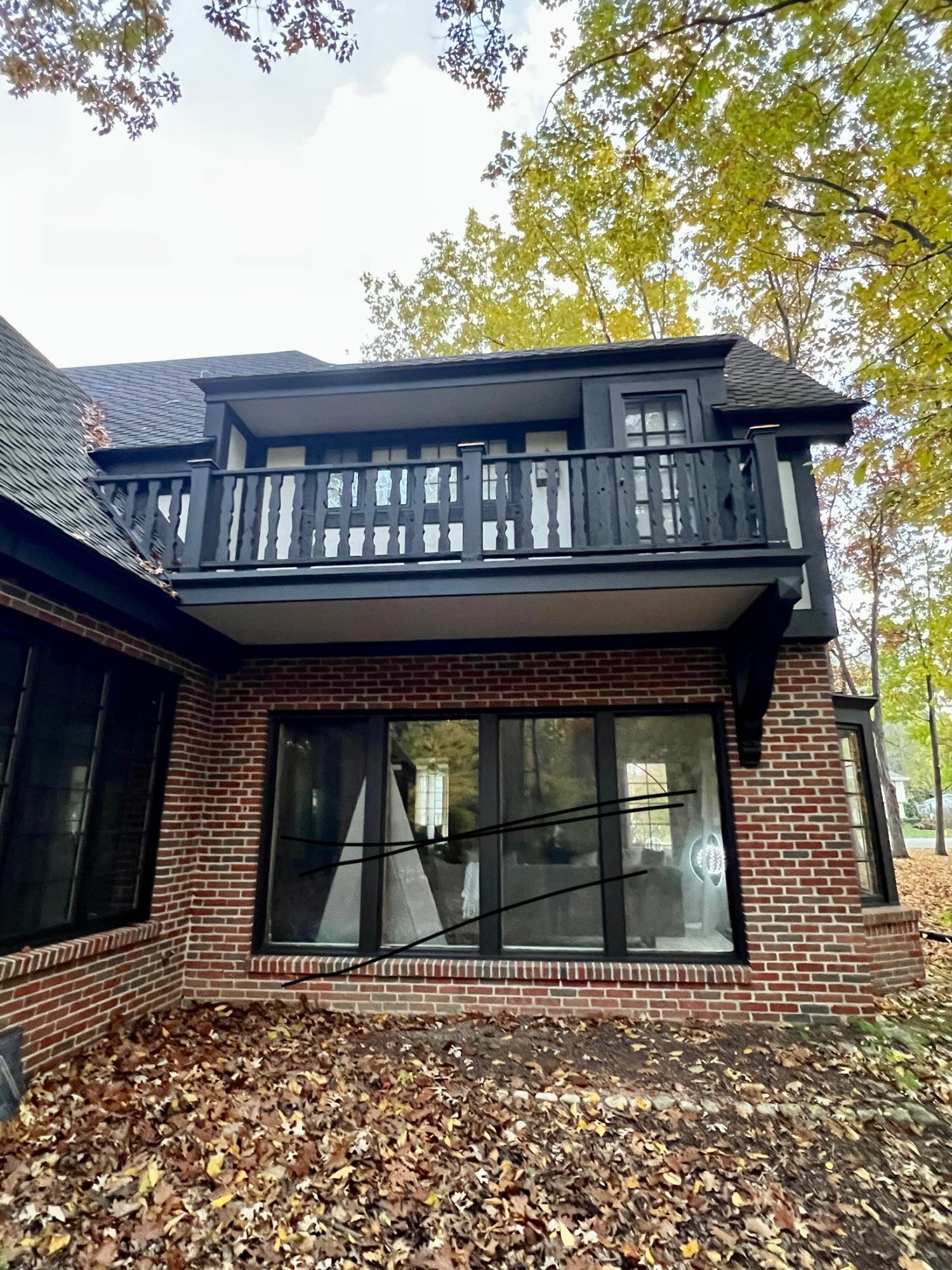 Rear of Tudor home showing freshly painted dark balcony, railing, and trim on brick
