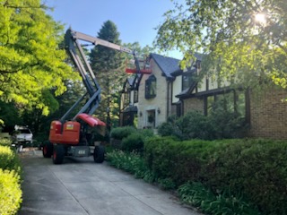 Boom lift reaching upper gables of Tudor-style home during exterior painting project