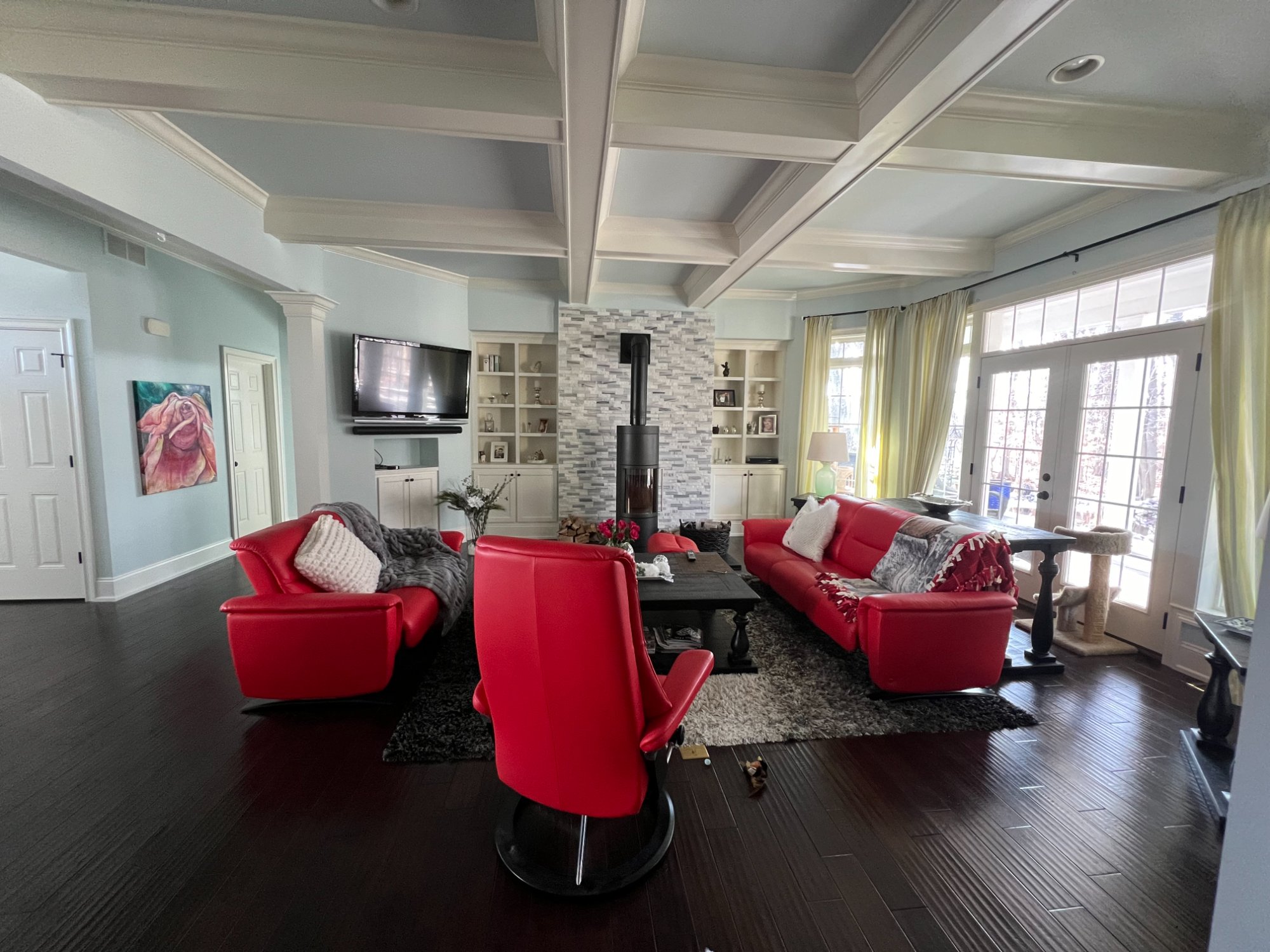 Open-concept living room with coffered ceiling, sage green walls, white built-ins and trim