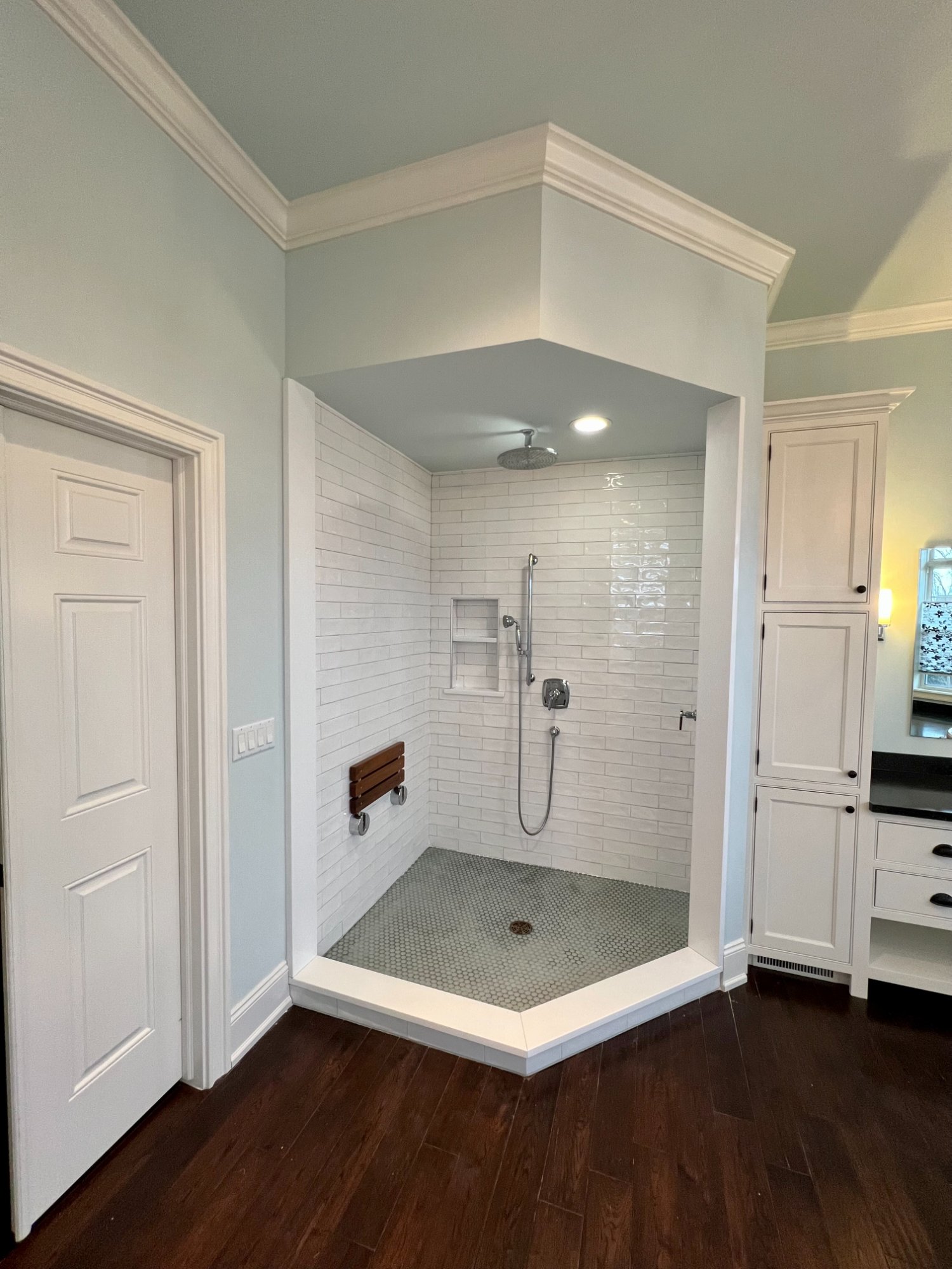 Corner walk-in shower nook with painted sage ceiling, white subway tile, and crown molding detail