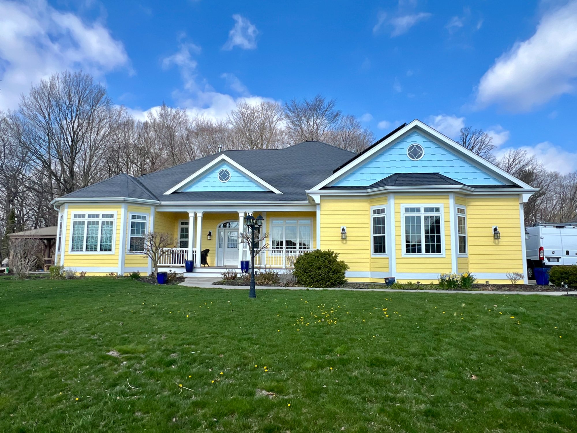 Yellow ranch home front view showing blue gable shingles and white porch railing