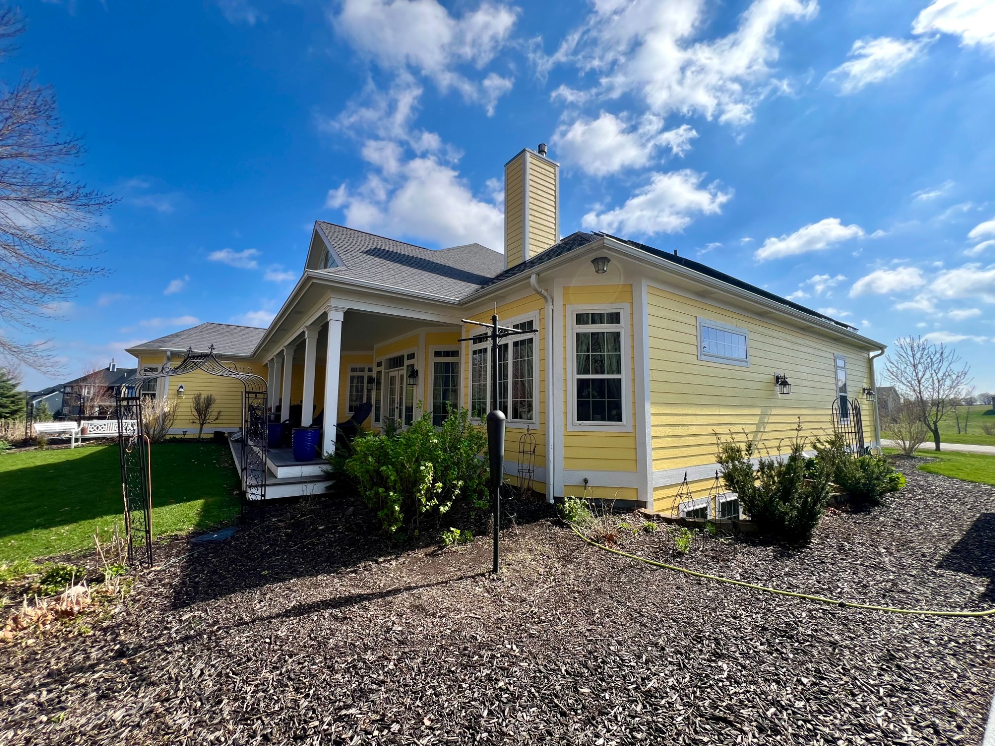 Yellow ranch home side and rear view showing chimney and landscaping