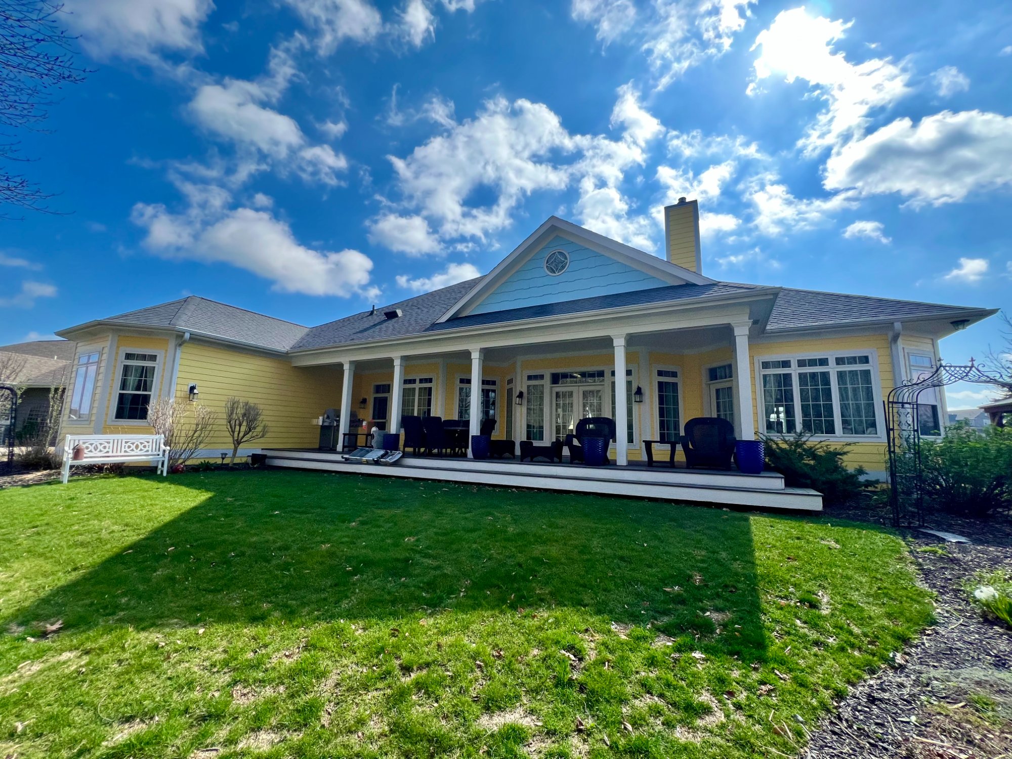 Rear view of yellow ranch home showing covered porch with white columns and blue gable accent