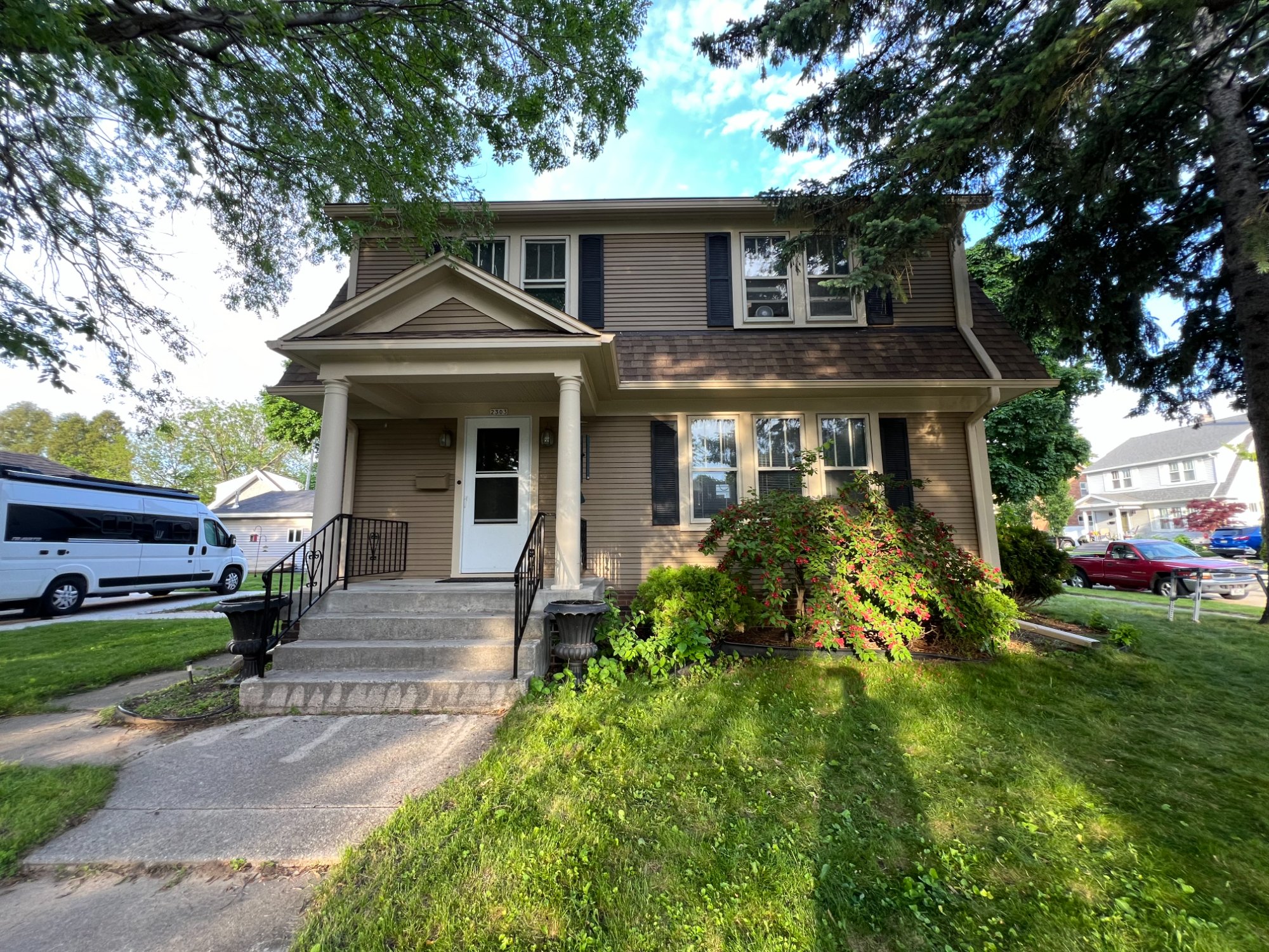 Two-story colonial home with fresh tan siding, dark shutters, and white trim
