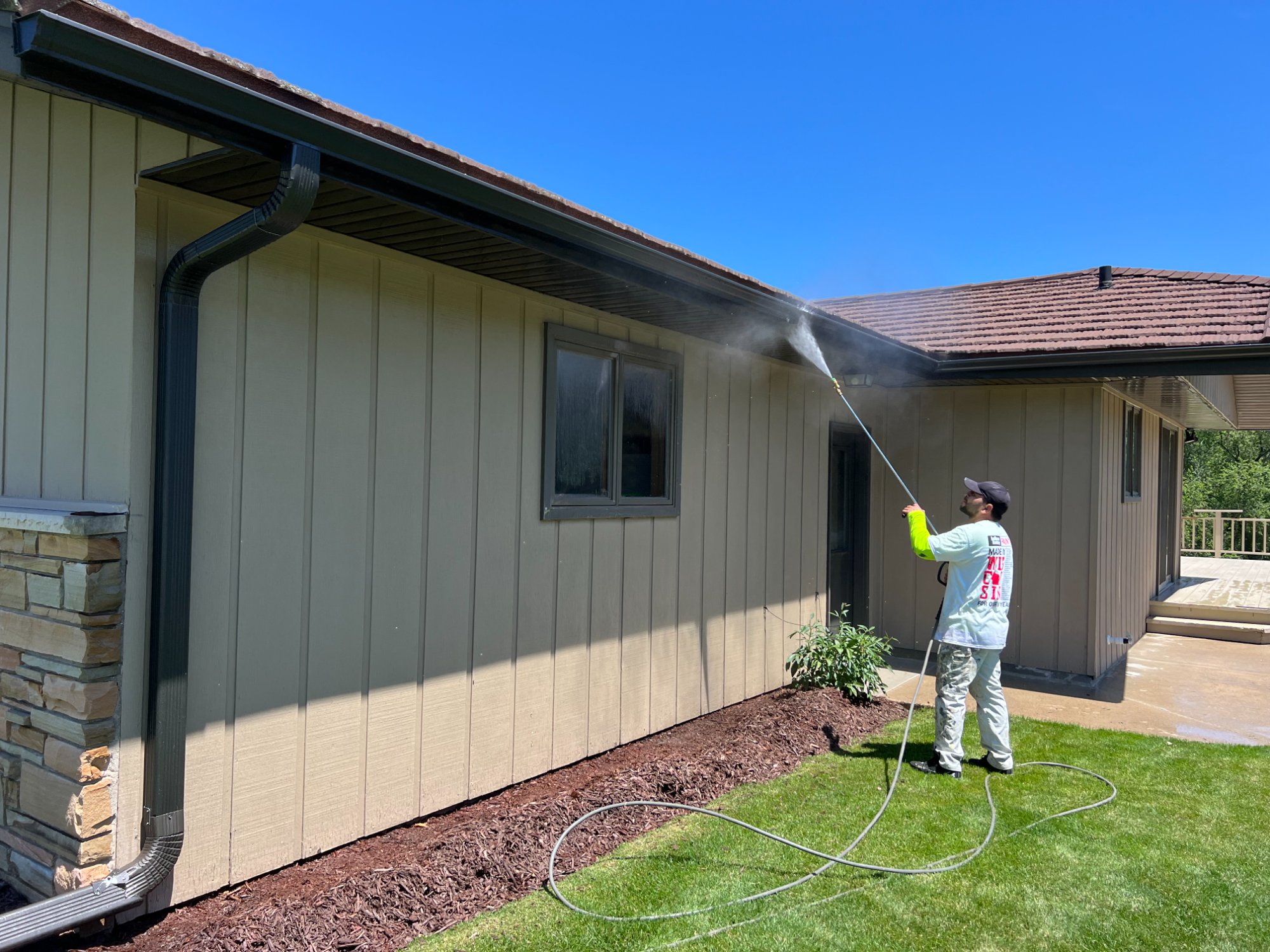 Worker power washing exterior board-and-batten siding of ranch home on sunny day