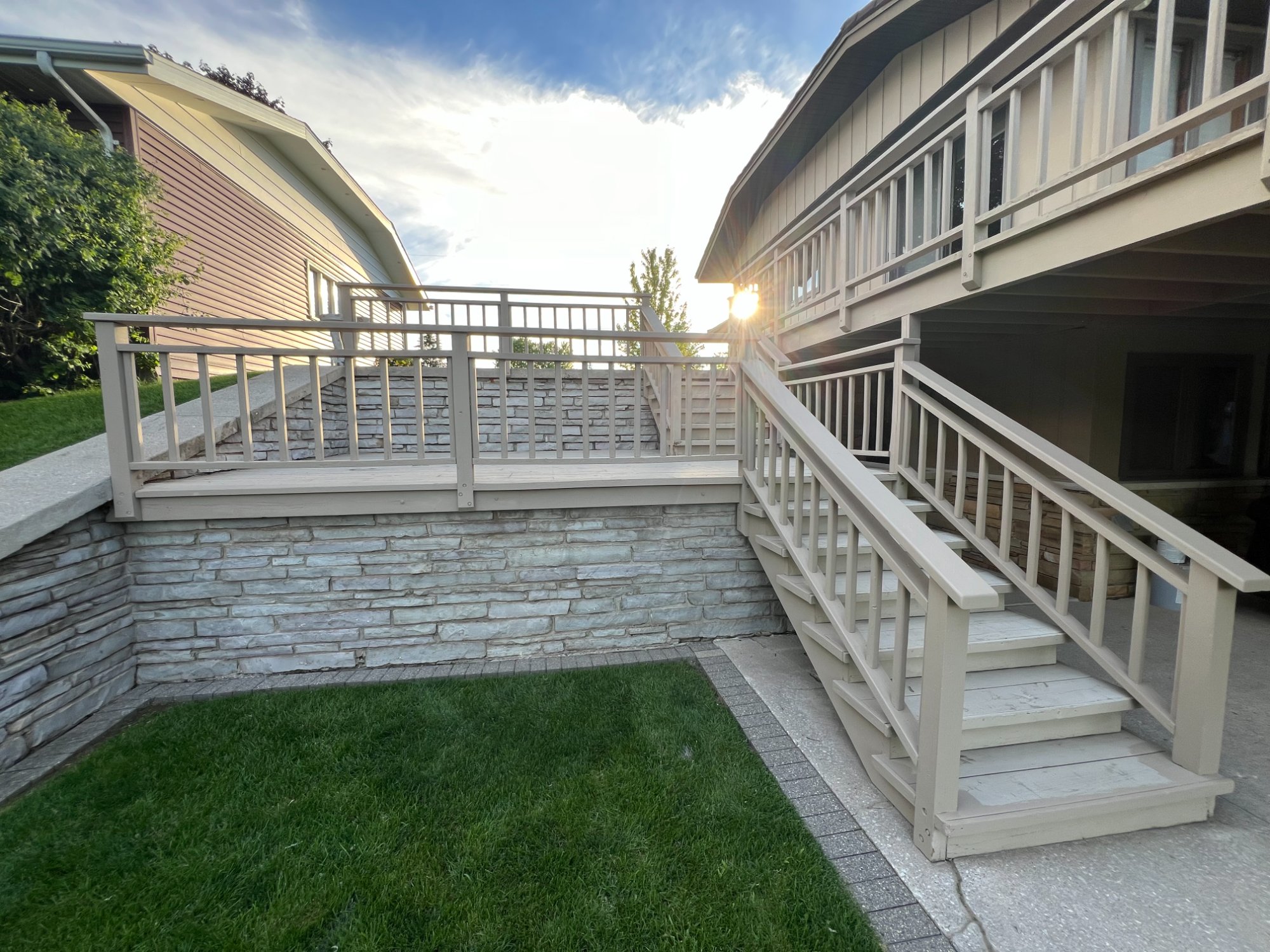 Freshly painted deck stairs and railings at sunset with stone retaining wall