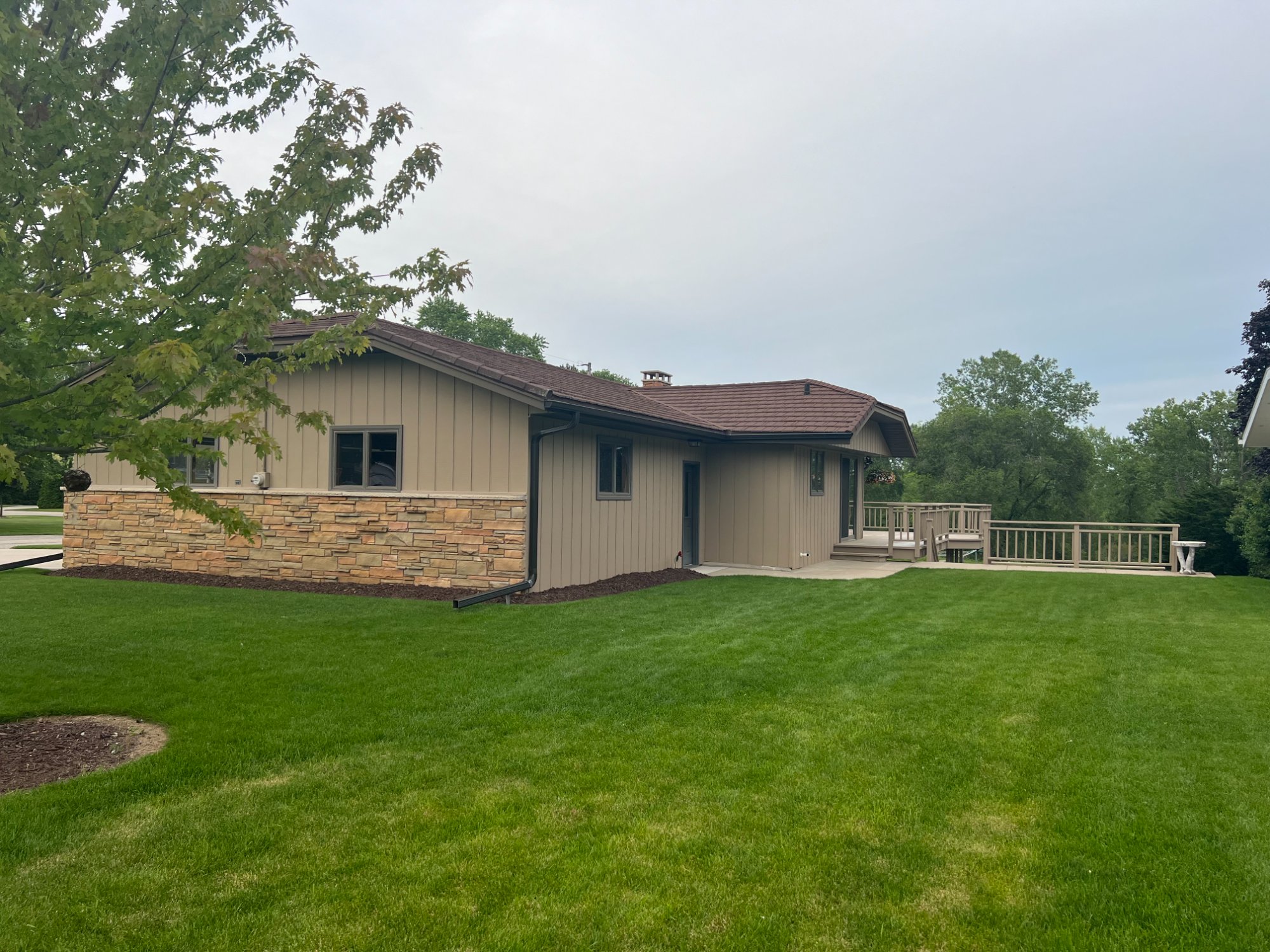 Side view of ranch home showing freshly painted board-and-batten siding with stone veneer base